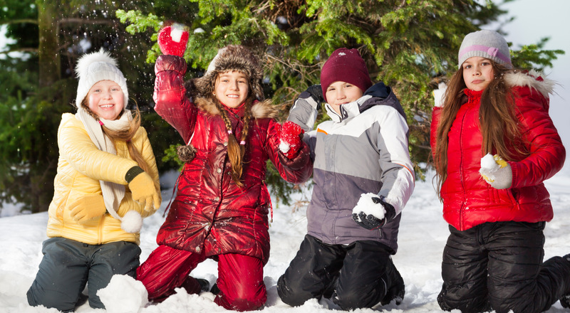 Fyra glada barn står på knä i snön och kastar snöboll. Foto.