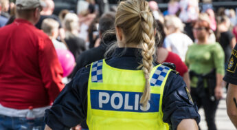 Kvinnlig polis står vid en folksamling med ryggen mot kameran. Foto.
