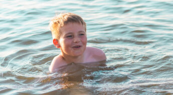 Glad pojke badar i sjö. Foto.