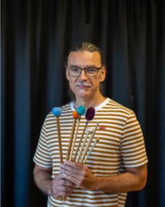 Man med glasögon håller i trumpinnar. Foto.