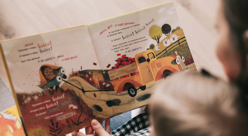 Ett litet barn sitter i ett knä och tittar i en bok