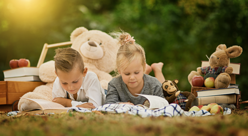 Två barn ligger på en gräsmatta och läser