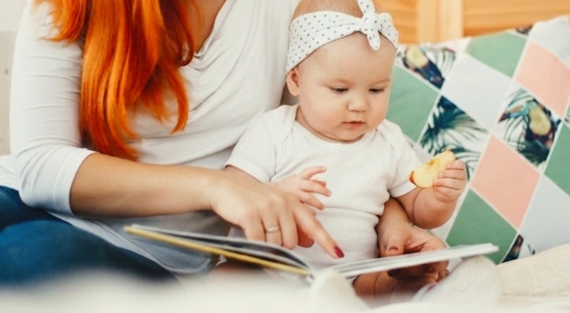 Litet barn sitter med sin mamma och tittar i en bok