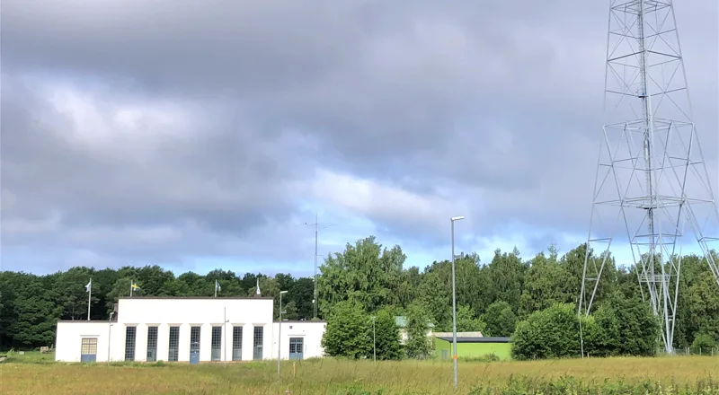 Vit byggnad syns på avstånd och intill syns en radiomast. Foto.