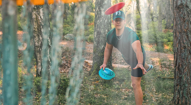 Ung man kastar disc mot discgolfkorg.