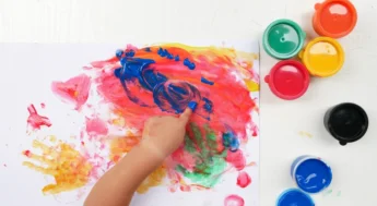 En barnhand målar med färg på papper. Foto.