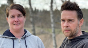 Korthårig kvinna och man står bredvid varandra och tittar in i kameran. Foto.