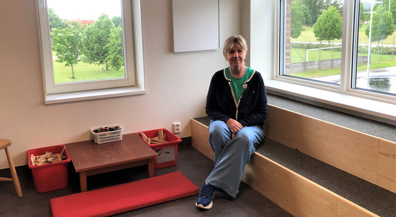 Kvinna sitter intill fönster i ett rum på förskolan Råssnäs. Foto.