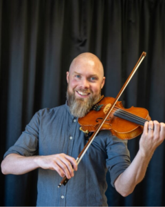 Man med skägg håller i fiol. Foto.