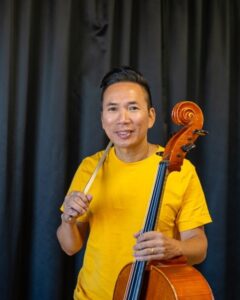 Man med mörkt hår håller i stränginstrument. Foto.