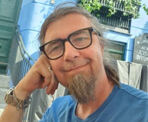 Man med glasögon och skägg tittar in i kameran. Foto.