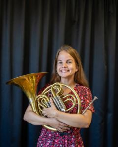 Kvinna håller i mässingsinstrument. Foto.