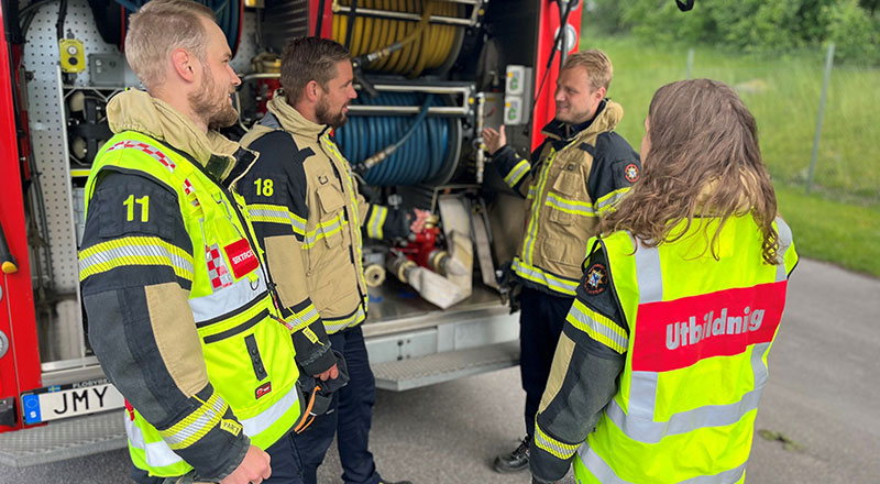 Fyra medarbetare från räddningstjänsten står vid ett räddningsfordon. Foto.