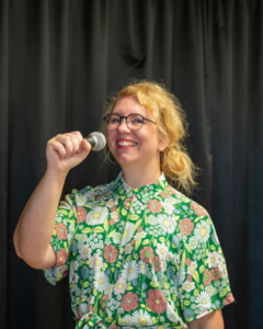 Blond kvinna håller i mikrofon. Foto.