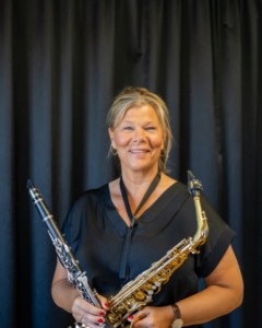 Blond kvinna håller i blåsinstrument. Foto.