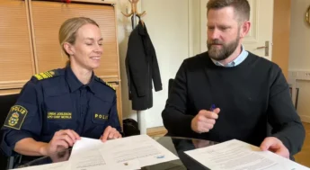 Kvinna med polisuniform och man sitter vid bord och skriver under papper. Foto.