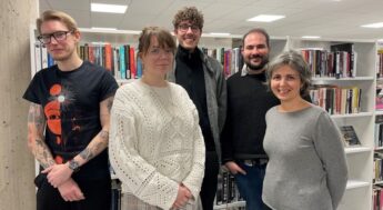 Tre män och två kvinnor står i ett bibliotek. Foto.