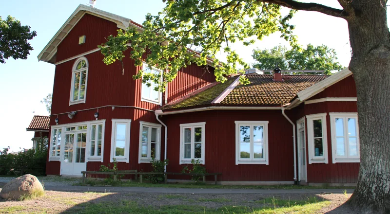 Röd träbyggnad omgiven av träd. Foto.