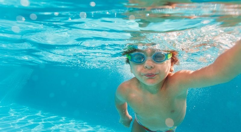 pojke med simglasögon simmar under vattnet